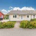 Ein hellgelbes Ferienhaus mit Garten und Parkplatz. Ein schwarzes Auto steht vorne.