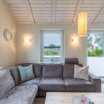 Wohnzimmer mit Ecksofa, Holzdecke und Fenstern zum Garten.