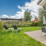 Garten mit Liegen und Tisch unter einem Schirm. Hinterhof mit Gras und Bäumen.