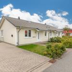 Ein hellbeiges Ferienhaus mit Garten und Terrasse unter blauem Himmel.