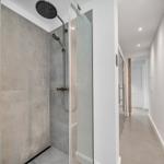 Duschkabine mit Glaswand und Duschbrause. Flur mit weißen Wänden und Boden.