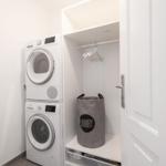 Waschmaschine und Trockner in weißer Wandnische mit Kleiderständer und Wäschekorb.