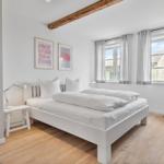 Schlafzimmer mit weißem Bett, Holzboden und Fenster mit Blick.