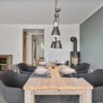 Esstisch mit sechs Stühlen und Holzoberfläche. Hängelampe und Kaminofen im Hintergrund.