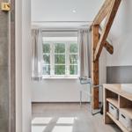 Badezimmer mit Dusche, Waschbecken und Holzrahmenspiegel. Holzbalken und Fenster mit Blick auf Bäume.