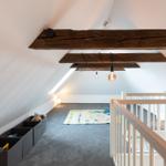 Dachgeschosszimmer mit Spielteppich, Holzbalken und Spielzeugboxen