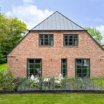 Rotes Backsteinhaus mit dunklen Fenstern und Terrasse im Garten.