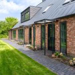 Rotes Backsteinhaus mit schwarzem Dach und Glasfronten. Pflasterweg und grüner Rasen.