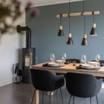 Esstisch mit sechs Stühlen und moderner Hängelampe. Im Hintergrund steht ein Holzofen.