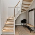 Treppe mit Holzstufen und moderner Beleuchtung. Eingangsbereich mit Sitzgelegenheit und Kleiderständer.