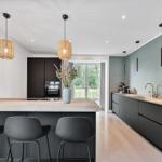 Moderne Küche mit Kücheninsel, schwarzen Schränken und Holzboden. Durchgang zur Terrasse.