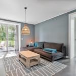 Wohnzimmer mit Sofa, Tisch und Fenstern zum Garten.