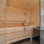 Sauna mit Holzbank und Glaswand. Heizung und Eimer sind sichtbar.