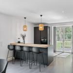 Moderne Küche mit Kücheninsel und Sitzgelegenheit. Durchgang zur Terrasse mit Gartenansicht.