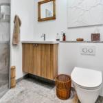 Badezimmer mit Dusche, Waschbecken und Toilette. Holzschrank, Spiegel und Wandbild.