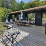 Terrasse mit Tisch, Stühlen und Grill. Holzhaus mit grüner Umgebung.