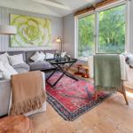 Wohnzimmer mit Sofa, Teppich und großen Fenstern. Wandbild und Deckenleuchte sichtbar.