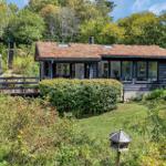 Ein Haus mit Grasdach, Terrasse und Garten. Umgeben von Bäumen und Sträuchern.