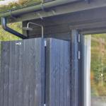 Außen-Dusche mit Holzabtrennung und Dachrinne. Grüne Umgebung sichtbar.
