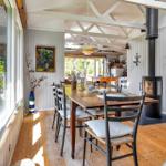 Esszimmer mit Holztisch, Stühlen und Kaminofen. Große Fenster und helles Holzfußboden.