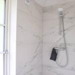 Dusche mit Marmorwand und Duschbrause. Fenster mit Glastüren.