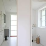 Badezimmer mit Dusche, Waschbecken und Fenster. Weiße Wände und Bodenfliesen.