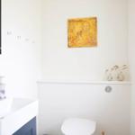 Badezimmer mit Waschbecken, Spiegel, Toilette und Fenster.