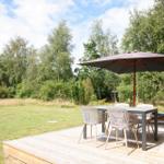 Terrasse mit Tisch, Stühlen und Sonnenschirm. Grasfläche und Bäume im Hintergrund.