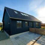 Moderne dunkelblaue Hütte mit Dachfenstern und Steinplattenhof.