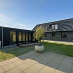 Moderne Villa mit großem Garten und Terrasse. Große Fenster und ein Balkon sind sichtbar.