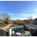 Terrasse mit Blick auf Garten und Nachbarhäuser unter blauem Himmel.