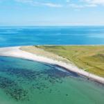 Aerielansicht einer Halbinsel mit Strand und grünen Hügeln. Meer und Himmel sind klar.