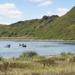 Zwei Boots mit Personen auf ruhigem Wasser vor grünen Hügeln.