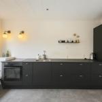 Küche mit schwarzen Schränken, Arbeitsplatte und Fenster mit Sitzbank.