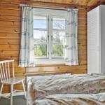 Schlafzimmer mit Holzwand, Fenster, Gardinen, Bett und Stuhl.