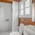 Badezimmer mit Dusche, Toilette und Waschbecken. Holzwände und Fenster.