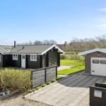 Holzhaus mit Garage und gepflastertem Weg. Grünflächen und Zaun sichtbar.