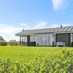 Ein Haus mit dunklem Holz und großen Fenstern steht auf einer grünen Wiese.