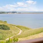 Weitläufiger Blick auf ruhiges Wasser und grüne Dünen mit Wanderweg.