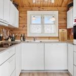 Küche mit weißen Schränken, Holzwand und Fenster mit Vorhang.