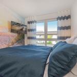 Schlafzimmer mit Bett, Fenster und Strandmotiv an der Wand.