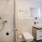 Badezimmer mit Dusche, Waschbecken und Toilette. Wanddekoration mit Anker-Motiv.