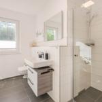 Badezimmer mit Dusche, Waschbecken und Toilette. Fenster mit Blick nach draußen.