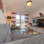 Wohnzimmer mit Sofa, Fernseher und Fenster mit Gardinen.