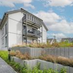 Modernes Mehrfamilienhaus mit Balkonen und gepflastertem Weg.