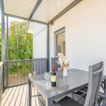 Terrasse mit Tisch, Stühlen, Weinflasche und Blumen. Blick in den Wald.