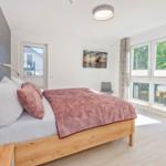 Schlafzimmer mit Bett, Fenstern und Wandbild.