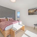 Schlafzimmer mit Bett, Nachttisch und Stuhl. Wandbild und Fenster sichtbar.