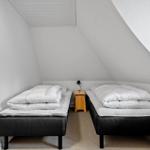 Zwei Matratzen mit weißen Decken in einem Dachzimmer mit schrägen Wänden und einem kleinen Nachttisch.