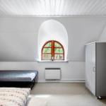 Zimmer mit Bett, Schrank und Bogenfenster mit Blick auf Grün.